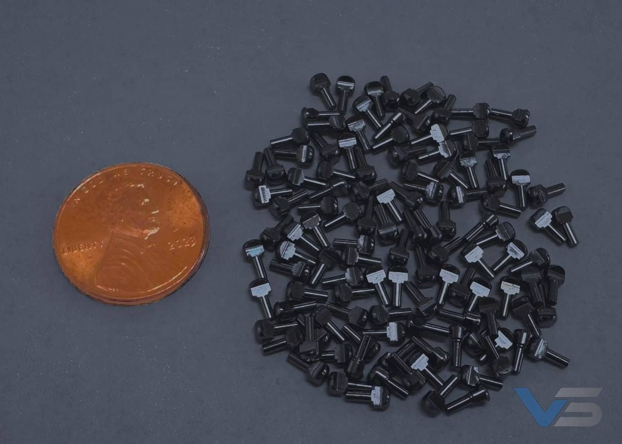 Batch of micro-machined stainless pins beside a penny for scale